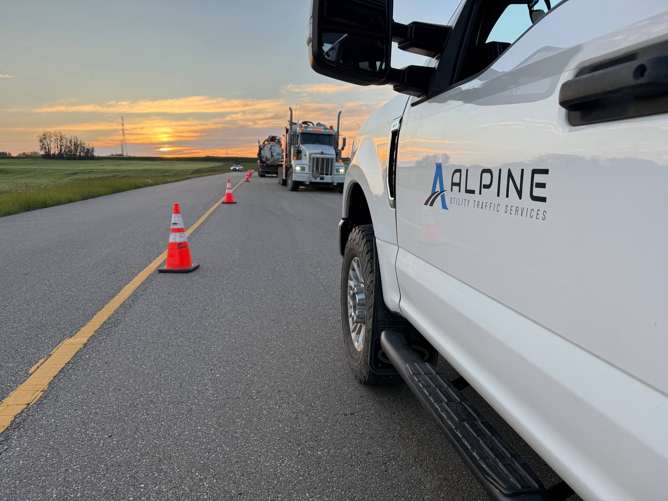 Alpine Utility Traffic Services truck staged beside a protected work zone at sunset